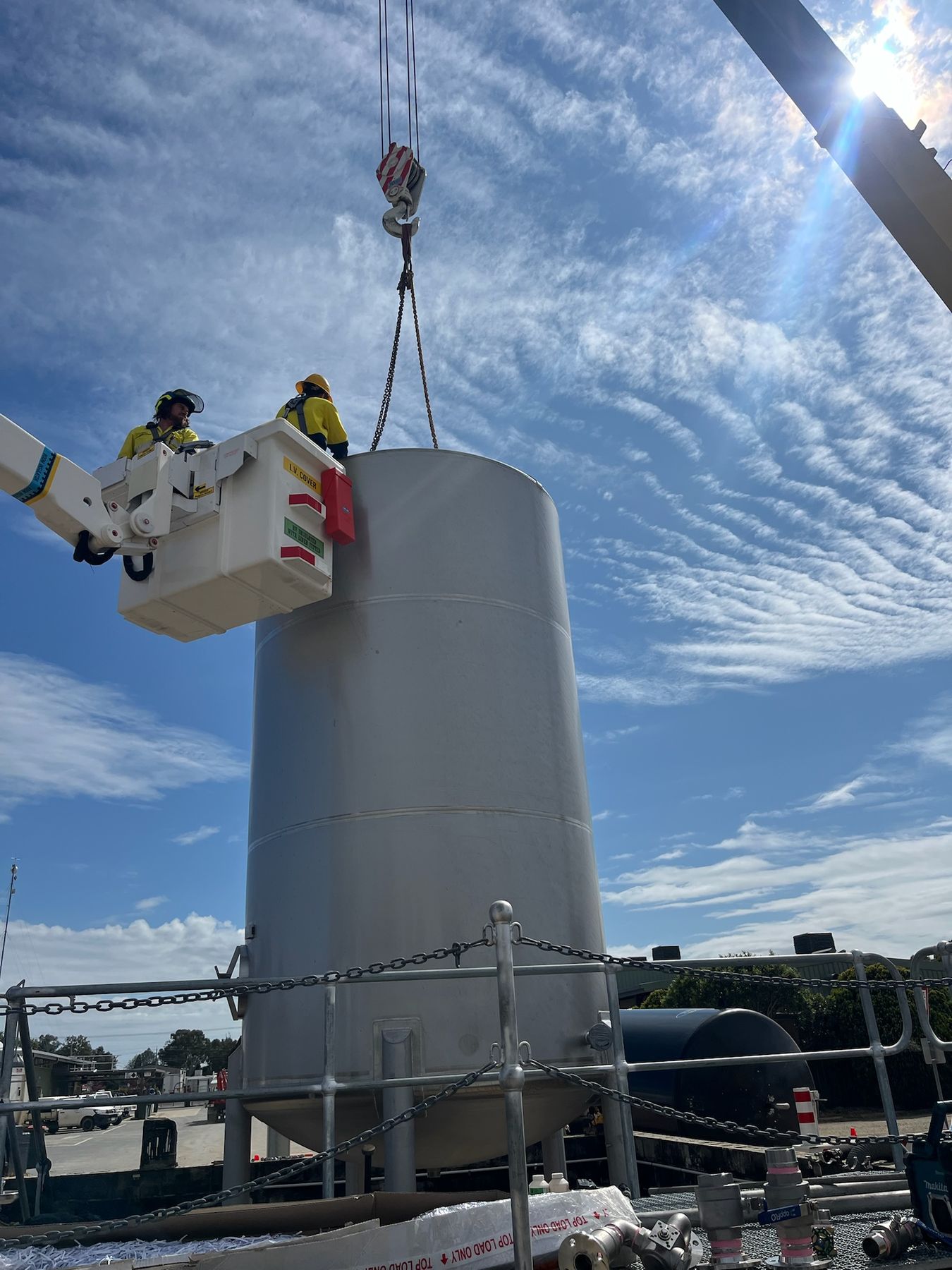 Crew in an elevated work platform positioning a tank lifted by crane