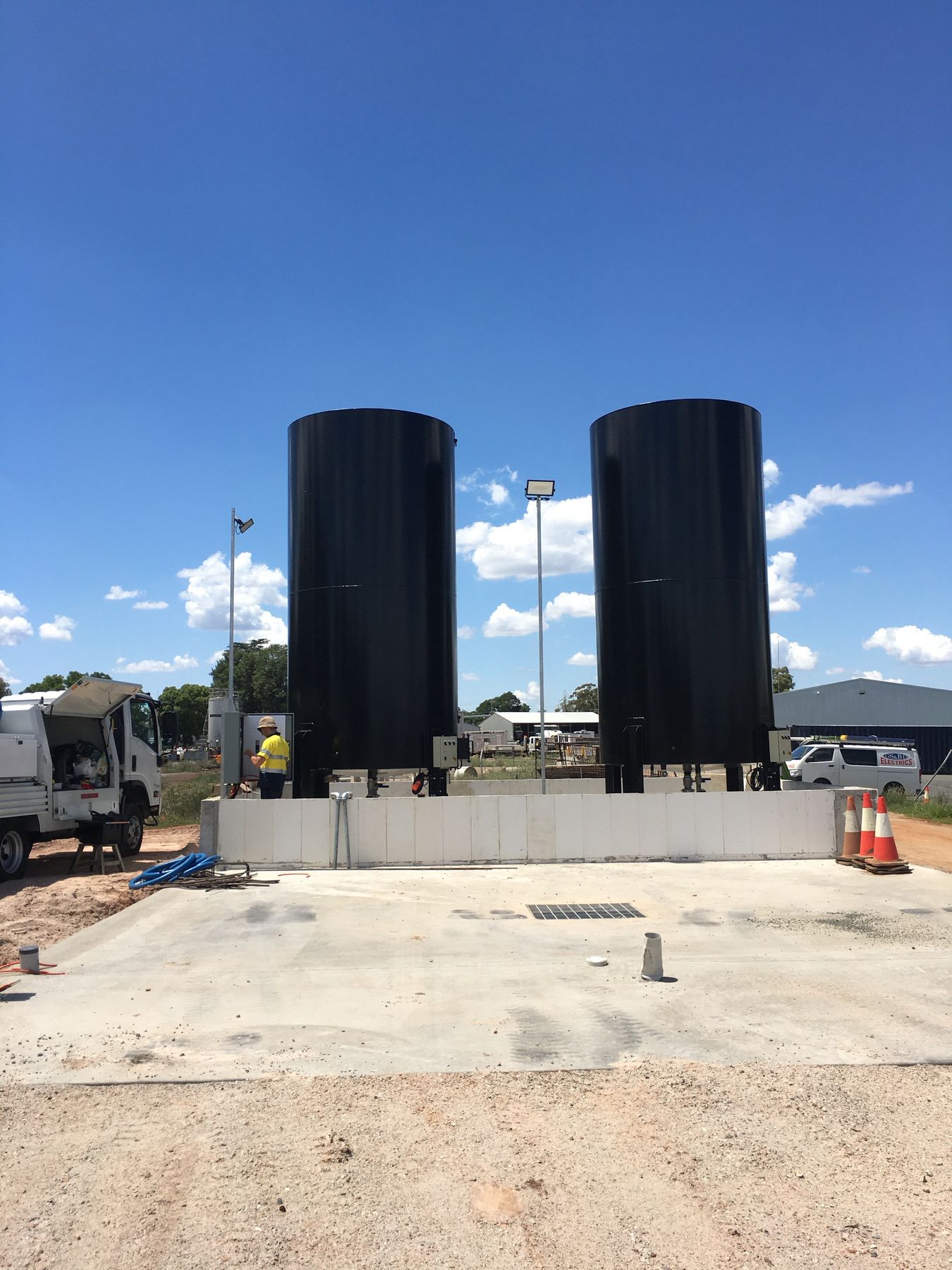 Two black storage tanks inside a concrete containment wall