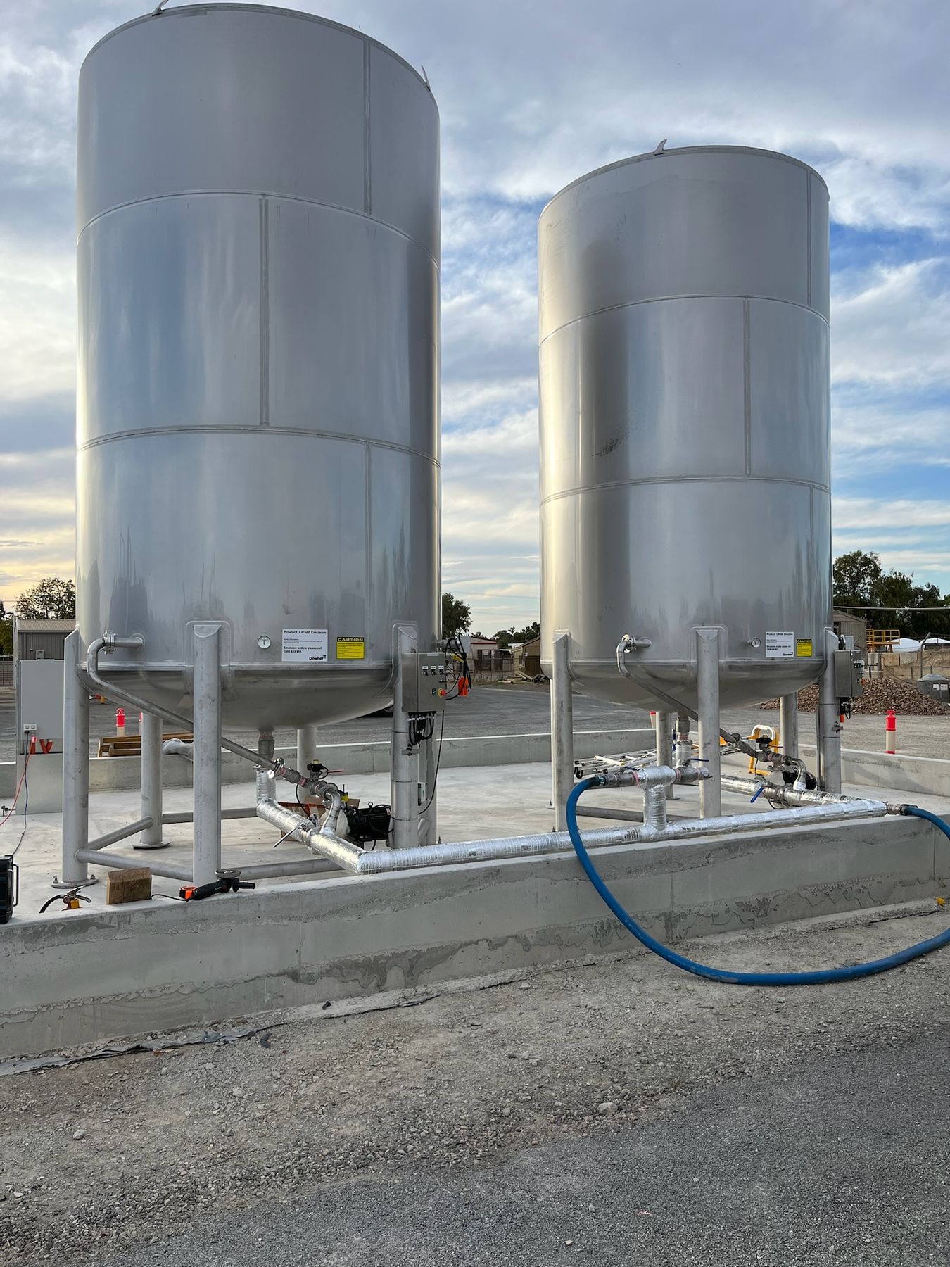 Two stainless steel emulsion tanks with insulated pipework on a concrete containment slab